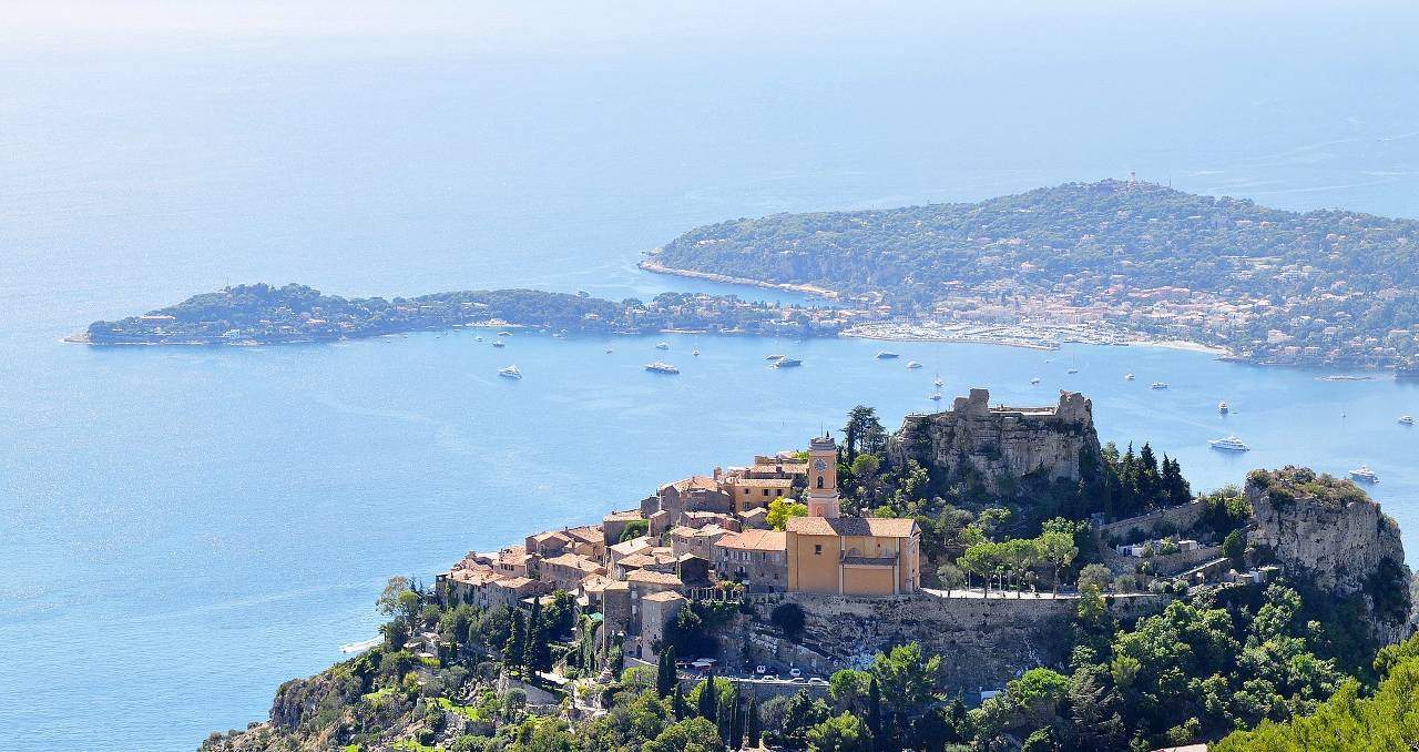 The village of Èze, with its church “Our Lady of Assumption” (Notre-Dame de l’Assomption) and its castle in the foreground, and the Cape Ferrat in the background.